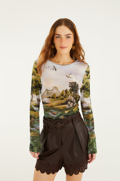 Long-sleeve ruched top featuring a countryside landscape in muted greens and pastels, paired with brown shorts.