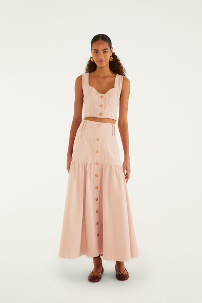 Cotton twill pink denim maxi skirt with a tiered ruffle hem, button front, and side pockets, worn with a matching crop top.