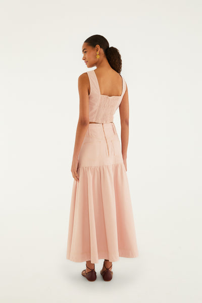 Pink denim maxi skirt with a tiered ruffle hem and copper-toned button details, worn with a matching top.