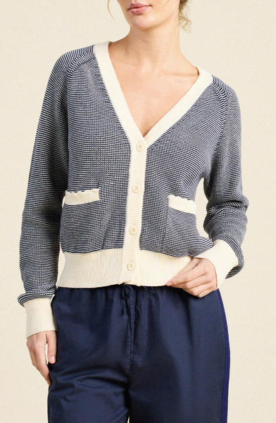 Navy and ivory cotton cardigan sweater with a deep V-neck, button front, and two front pockets, worn over dark trousers.