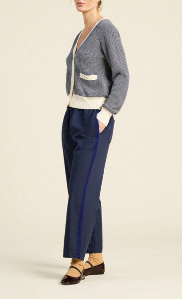 Navy cotton cardigan with ivory details, deep V-neck, long sleeves, and pockets, styled over navy trousers.